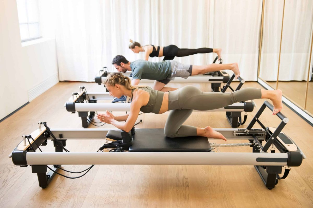 Group,Of,Friends,Doing,Pilates,Kneeling,Glutes,Exercises,On,Reformer